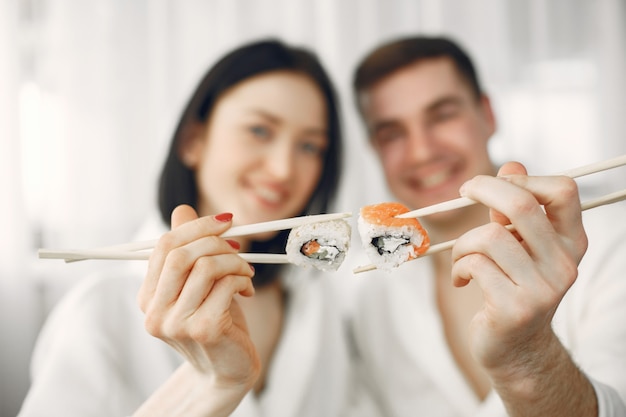 Pareja joven vistiendo albornoces comiendo sushi.