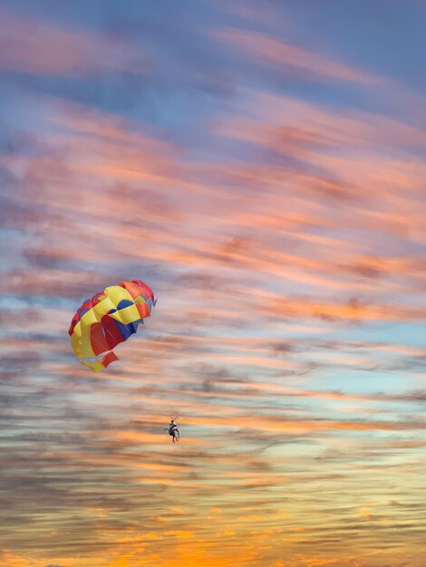 Foto una pareja joven está volando en el cielo azul usando un paracaídas de colores