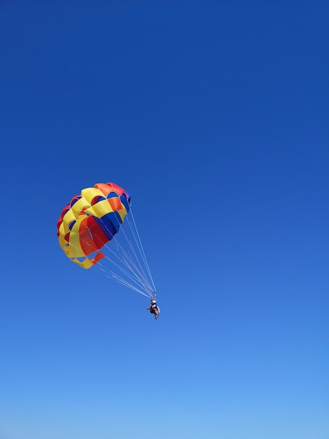 Foto una pareja joven está volando en el cielo azul usando un paracaídas colorido