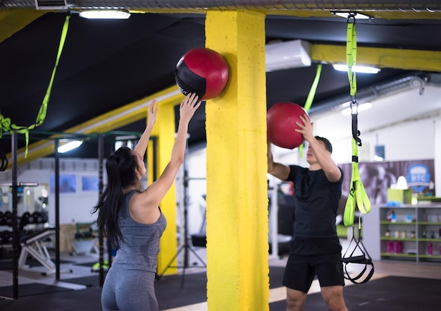 Pareja de jóvenes atletas que se resuelve con pelota médica en el gimnasio de fitness cruz