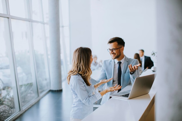 Pareja de jóvenes empresarios trabajando y discutiendo por computadora portátil en la oficina frente a su equipo