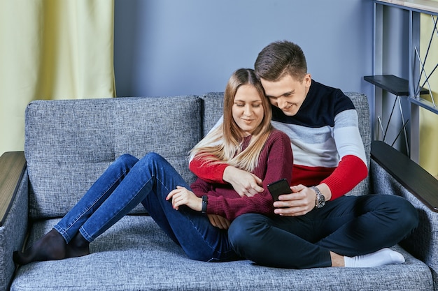 Pareja de jóvenes enamorados sentados en el sofá en un apartamento o dormitorio de estudiantes.