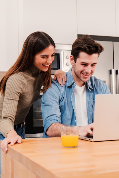 Una pareja de jóvenes felices verticales usando una computadora portátil para ver en la pantalla del portátil navegando por Internet disfrutando