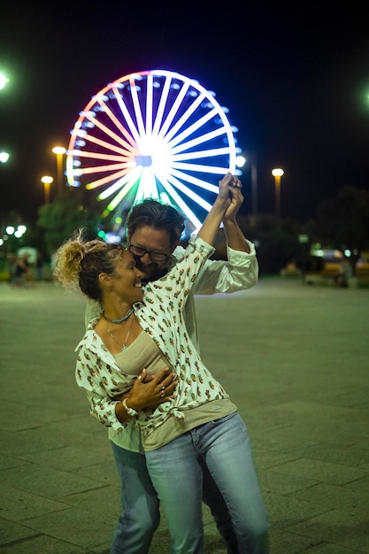 Una pareja de jóvenes maduros baila al aire libre con atracciones de luna park en el fondo Concepto de celebración y felicidad con un hombre y una mujer divirtiéndose juntos en la noche al aire libre La gente alegre celebra