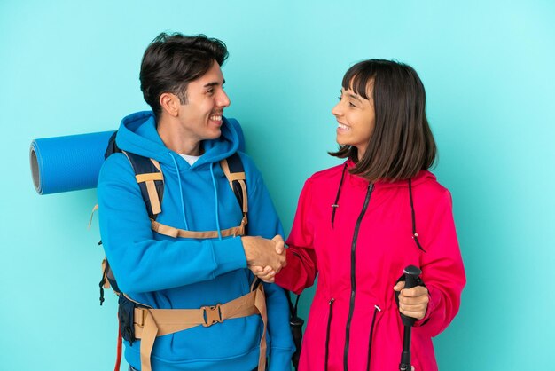 Una pareja de jóvenes montañeros aislados en un apretón de manos de fondo azul después de un buen trato