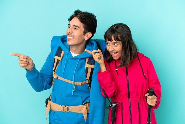 Una pareja de jóvenes montañeros aislados de fondo azul presentando una idea mientras miran sonriendo hacia