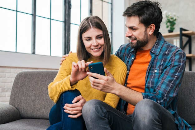 Pareja de jóvenes sentados juntos en el sofá usando un teléfono móvil