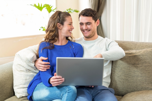 Pareja de jóvenes sentados en el sofá y usando una computadora portátil en la sala de estar