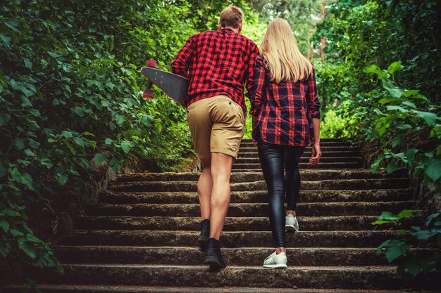 Pareja de jóvenes skaters casuales posando en la acera en un parque forestal.