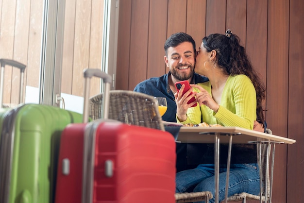 Pareja de jóvenes turistas desayunando en un hotel y mirando el teléfono móvil