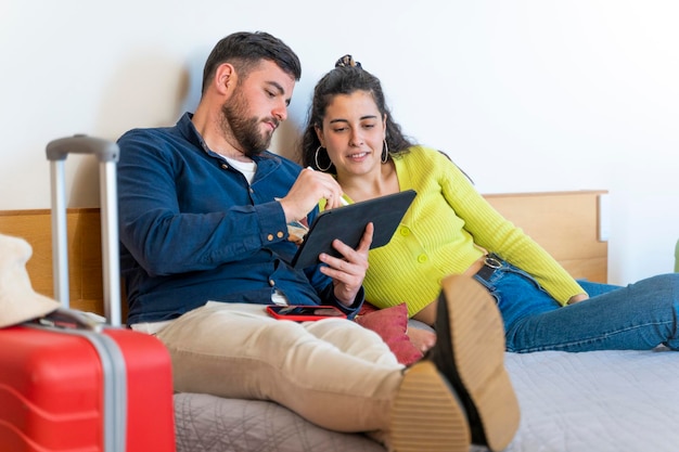 Pareja de jóvenes turistas dibujando en una tableta en la cama en una habitación de hotel