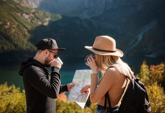 Pareja de jóvenes turistas, hombre y mujer, en ruta de senderismo en las montañas, sosteniendo el mapa y encontrando el camino en la naturaleza en un día soleado