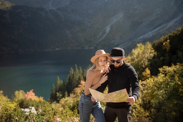 Pareja de jóvenes turistas, hombre y mujer, en ruta de senderismo en las montañas, sosteniendo el mapa y encontrando el camino en la naturaleza en un día soleado