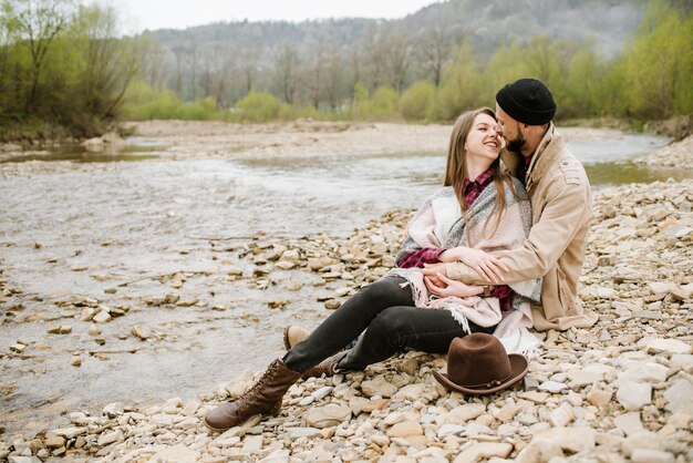 Pareja de jóvenes viajeros se abraza en el río de montaña en el fondo