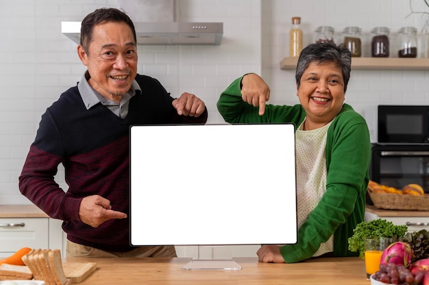Una pareja jubilada muestra una pantalla de computadora portátil vacía en la cocina Disfruten de una jubilación relajante juntos Espacio libre para comunicaciones publicitarias