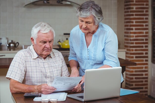Pareja de jubilados calculando facturas con laptop