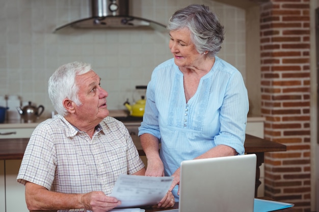 Pareja de jubilados discutiendo mientras calcula facturas con laptop