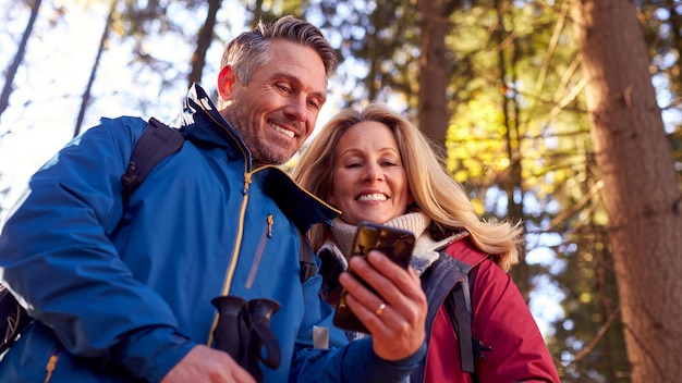 Pareja de jubilados maduros caminan en el campo de otoño o invierno usando el mapa o la aplicación de navegación en el teléfono móvil