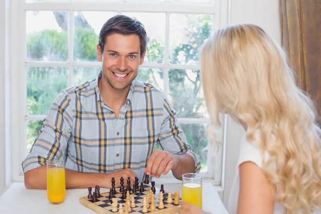 Pareja jugando al ajedrez mientras toma jugo de naranja en casa