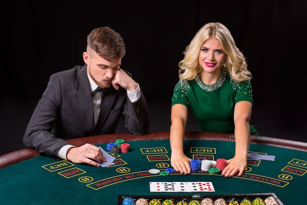 Pareja jugando al póquer en la mesa verde. La chica rubia y un chico de traje. fichas de apuestas con todo incluido