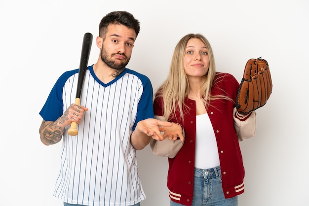 Pareja jugando béisbol sobre fondo blanco aislado teniendo dudas mientras levanta las manos y los hombros