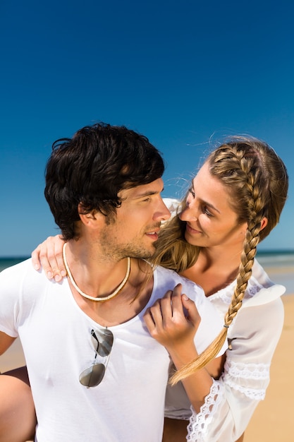 Pareja juguetona en la playa del océano disfrutando de sus vacaciones de verano, el hombre lleva a la mujer a cuestas