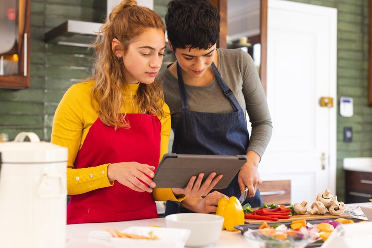 Foto una pareja lesbiana biracial enfocada usando una tableta y preparando verduras en la cocina