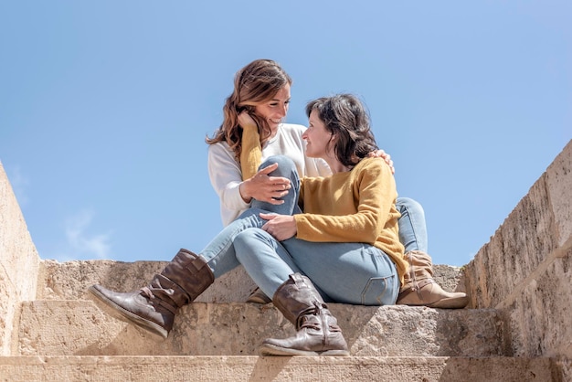 Una pareja de lesbianas abrazándose y mirándose a los ojos sentadas en las escaleras en el concepto de cielo azul de fondo del concepto de estilo de vida de relación de bisexualidad Lgbt