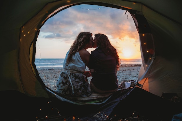 Una pareja de lesbianas se besan en una tienda en la playa durante la puesta de sol