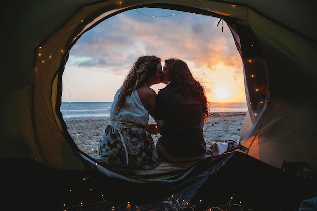 Foto una pareja de lesbianas se besan en una tienda en la playa durante la puesta de sol