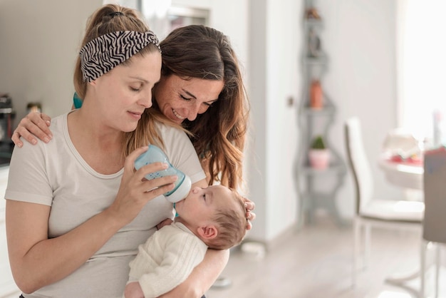 Una pareja de lesbianas dando una botella de leche a su bebé matrimonio gay padres gay y concepto de adopción