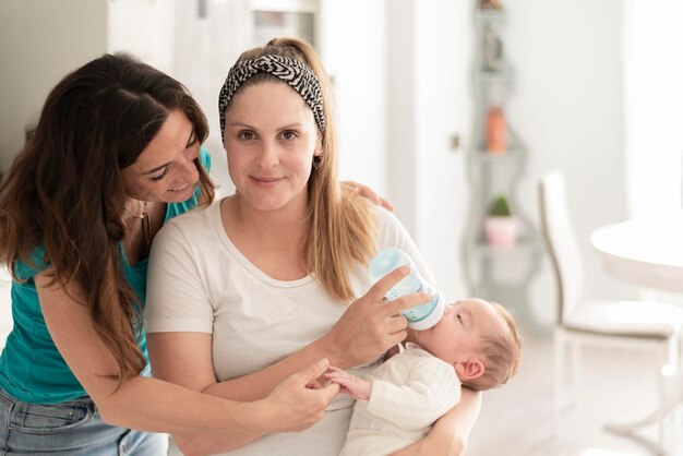 Una pareja de lesbianas dando una botella de leche a su bebé matrimonio gay padres gay y concepto de adopción