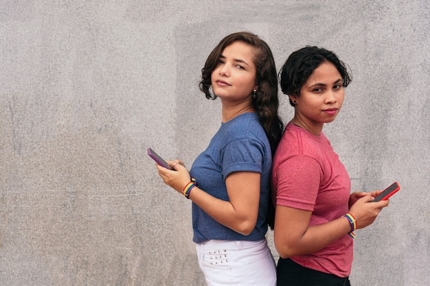 Pareja de lesbianas latinas con teléfono celular en la calle. Concepto LGBT