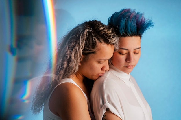 Foto pareja de lesbianas real abrazándose con un símbolo icónico del arco iris lgbt. étnica joven homosexual a punto de besar a una bella mujer punk con peinado mohawk azul.