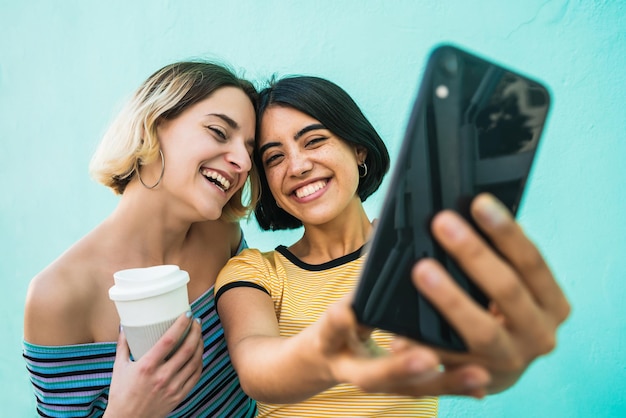 Foto una pareja de lesbianas sonrientes fotografiando mientras están de pie contra un fondo azul