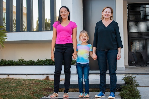 Pareja de lesbianas sosteniendo la mano de la hija adoptiva en la puerta de su casa. Pareja de lesbianas con hija. Concepto de adopción y diversidad