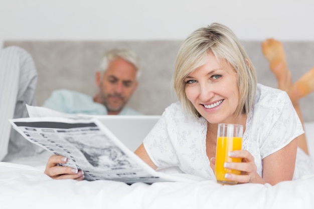 Pareja leyendo periódico y usando laptop en la cama