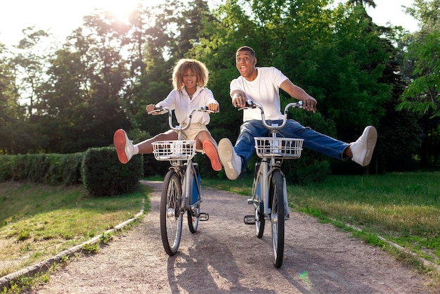 Una pareja loca afroamericana viaja rápidamente hacia adelante en el parque en bicicletas y grita