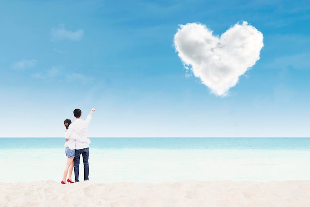Una pareja de luna de miel en la playa bajo una nube de corazón