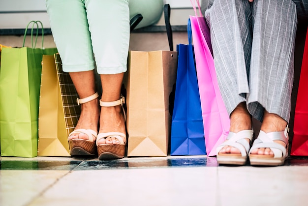 Pareja de madre e hija van de compras con muchas bolsas con regalos y más - dos personas sentadas en el banco del centro comercial