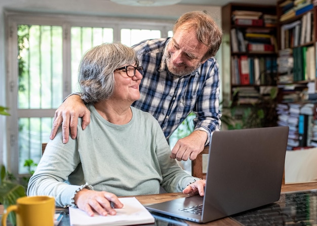 Pareja madura abrazada navegando por Internet en una computadora portátil en casa personas mayores de estilo lofstyle que usan una computadora portátil para comprar en línea