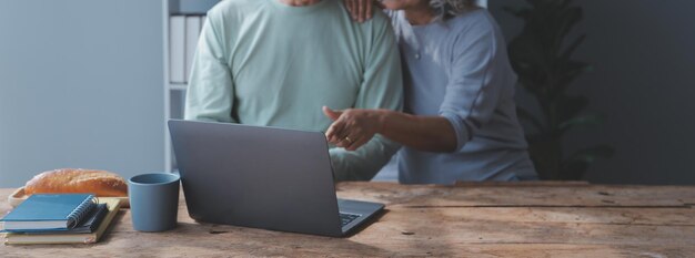 Foto pareja madura abrazada navegando por internet en una laptop en casa