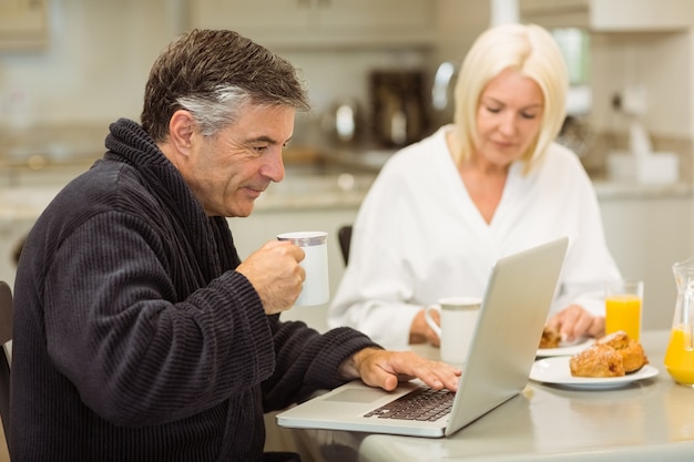 Pareja madura desayunando juntos hombre usando laptop
