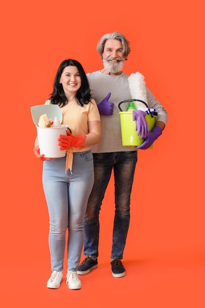 Foto pareja madura con productos de limpieza en la superficie de color