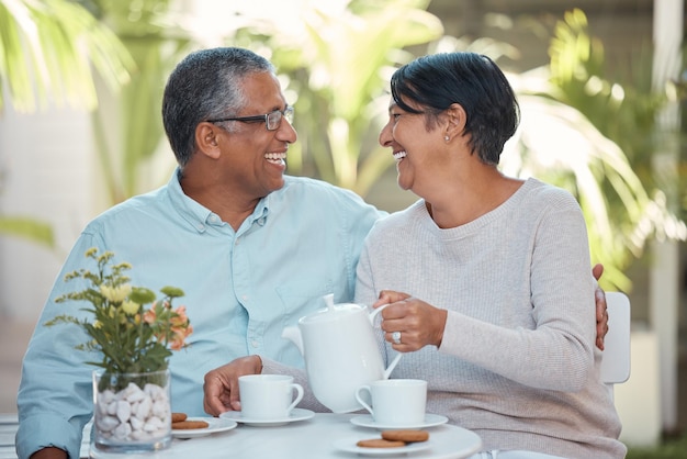 Pareja madura riendo bebiendo té y uniéndose en el patio trasero juntos relajarse y alegre al aire libre Hombre y mujer mayores disfrutando de la jubilación y su relación compartiendo una broma y un refrigerio a la hora del té