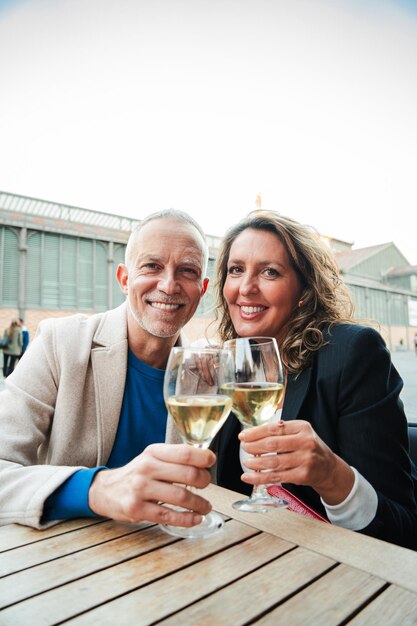 Una pareja madura vertical brindando copas de vino blanco sonriendo y mirando a la cámara de mediana edad casada