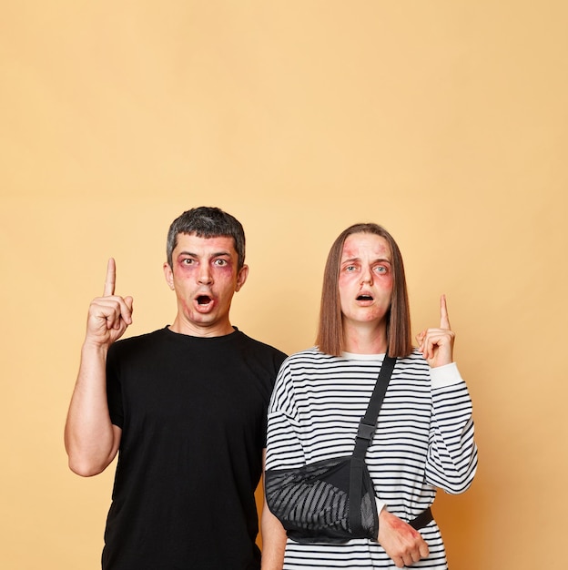 Foto una pareja maltratada, un hombre y una mujer, con hematomas aislados sobre un fondo beige, apuntando hacia el área del espacio de copia para la prevención de bandidos por texto