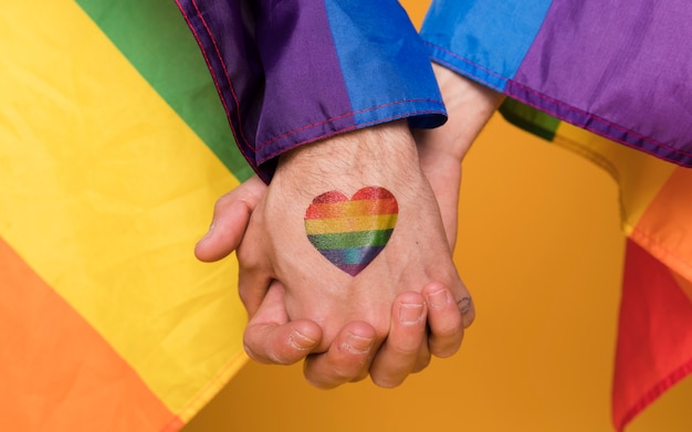 Pareja de manos de hombres homosexuales con imagen de corazón de arco iris