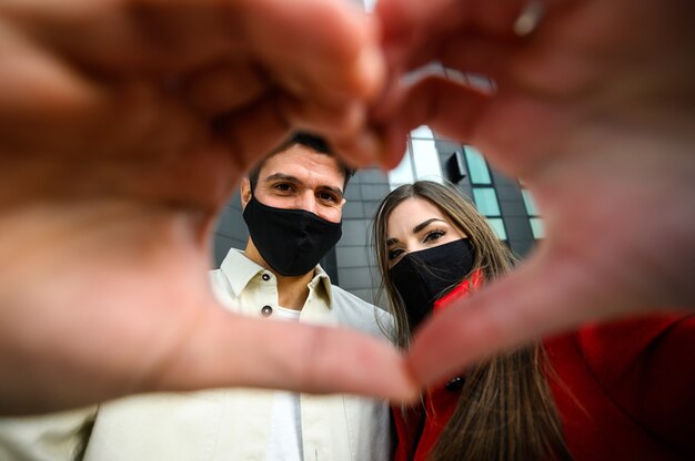 Pareja con máscaras y haciendo el signo de un concepto de corazón, covid y coronavirus