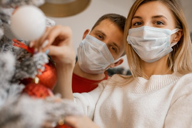 Pareja de máscaras médicas en su rostro cerca del árbol de Navidad